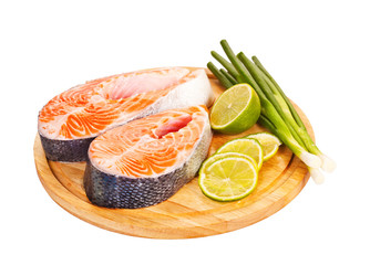 Two raw salmon steaks with lime and green onion on the cutting b