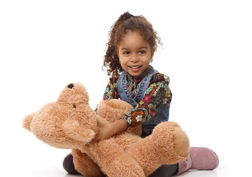 Cute ethnic girl playing with plush bear smiling