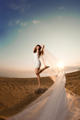 Fototapeta na wymiar Beautiful bride with a long veil on the beach at sunset