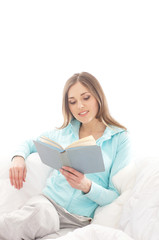 Fototapeta premium A young brunette woman reading a book on a white sofa