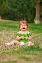 baby girl sitting on the green grass in the park and smiling