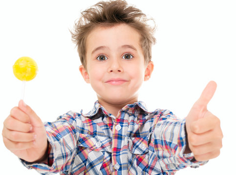 Little smiling boy shows thumb up with lollypop in hand