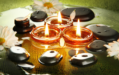 spa stones with flowers and candles in water on plate