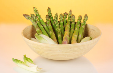 Fresh asparagus in wooden bowl on colorful background.