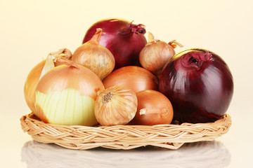 Ripe onions on wicker cradle on yellow background