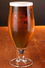 Glass of beer on wooden table on grey background