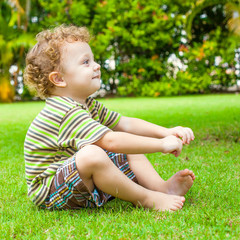 happy little boy sitting on the grass in the garden