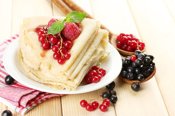 Delicious pancakes with berries and jam on plate on wooden