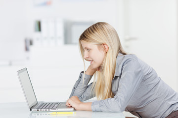 lächelnde frau im büro schaut auf laptop