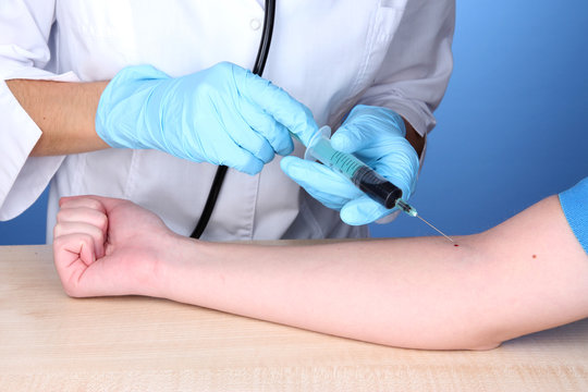 Nurse takes blood from the veins on blue background