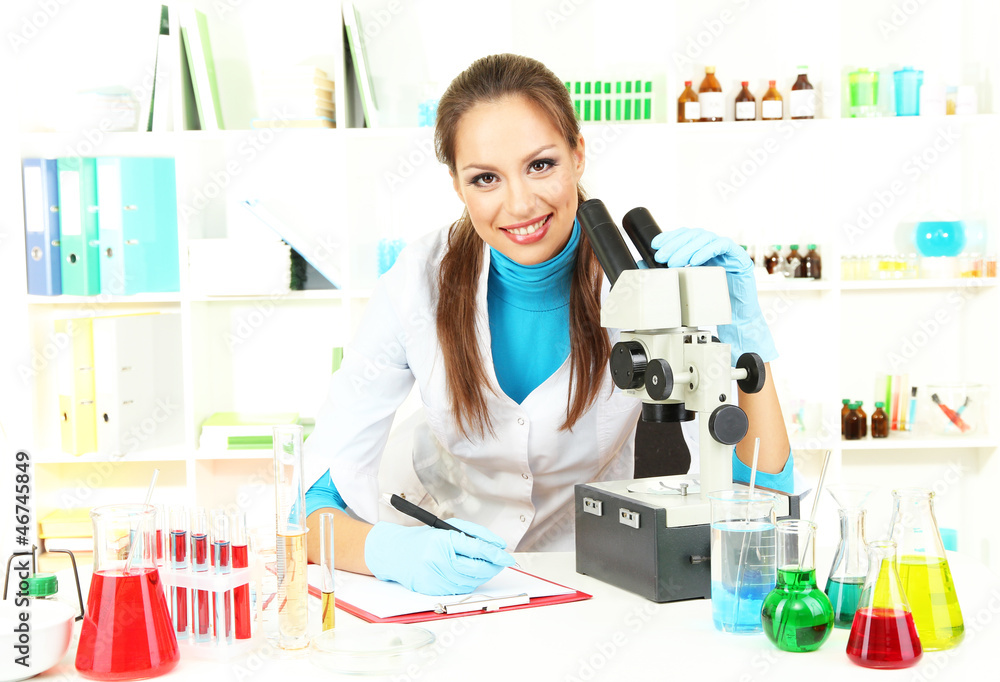 Wall mural young scientist looking into microscope in laboratory.