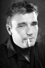 Smoking man with short brown hair. Black and white studio shot.