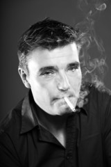 Smoking man with short brown hair. Black and white studio shot.