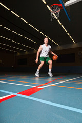 Tough healthy young man playing basketball in gym indoor.