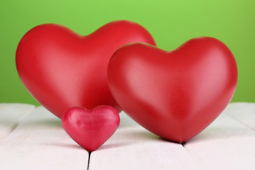 Decorative red hearts on white wooden table on green background