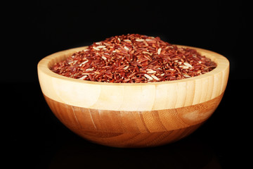 Red rice in wooden bowl isolated on black