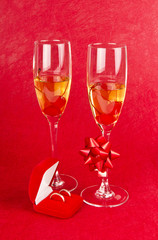 two glass goblets with champagne and jewelry on red background