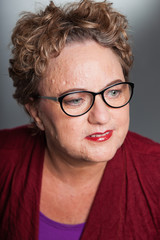 Smiling senior woman with short curly hair. Wearing glasses.