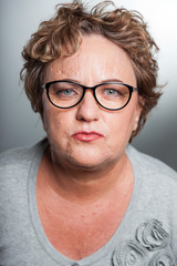 Serious senior woman with short curly hair. Wearing glasses.