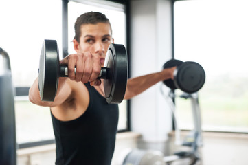 Fototapeta na wymiar Młody mężczyzna ćwiczeń z hantlami w siłowni, koncentrują się na wadze.