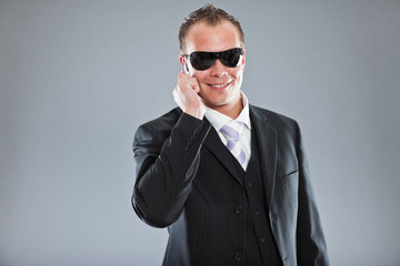 Macho business man calling with mobile phone wearing sunglasses.