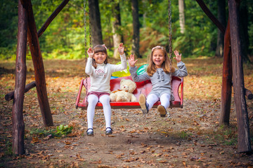 Happy little girlfriends on swing in park