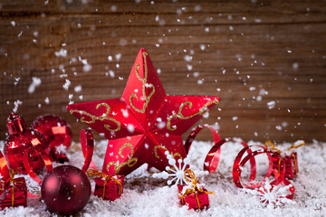 candle,holly,baubles,star and ribbons in snow before wood