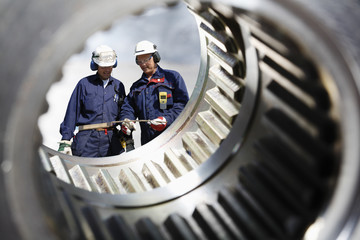 engineering and industry workers seen through giant gear axle