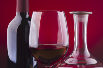 Botella de bino, copa y decantador sobre fondo rojo