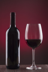 Botella de vino y copa sobre fondo rojo