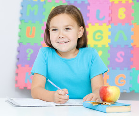 Little girl is writing using a pen