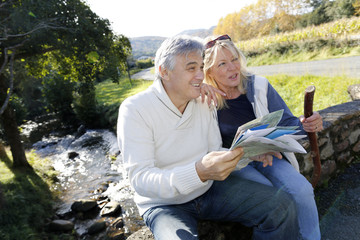 Senior couple sitting by river and looking at map