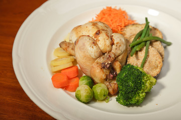 Dinner of vegetables and chicken on a plate and wooden table.