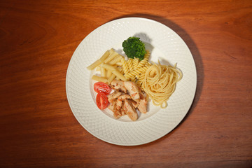 Dinner of vegetables pasta tomato and chicken on a white plate.