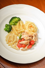Dinner of vegetables pasta tomato and chicken on a white plate.