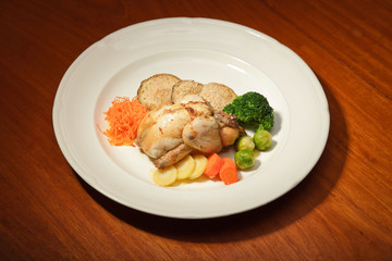 Dinner of vegetables and chicken on a plate and wooden table.