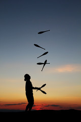 circus artist juggling with seven juggling clubs in sunset