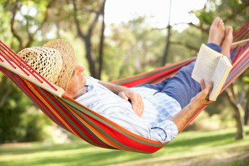 Senior Man Relaxing In Hammock With Book