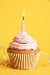 tasty birthday cupcake with candle, on yellow background