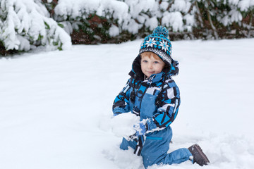 Fototapeta na wymiar Adorable toddler boy having fun with snow on winter day