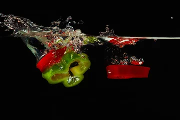 Fotobehang Plakken van rode en groene paprika& 39 s die met plons in het water vallen © Boris Bulychev
