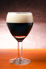 Glass of dark beer on wooden table with brown background.