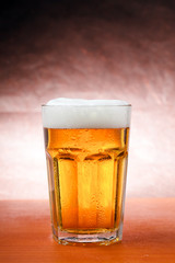 Glass of cold beer on wooden table with golden background.