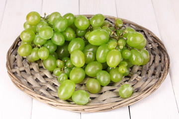 Ripe green grapes close-up on wicker cradle on wooden table