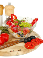 Fresh greek salad in glass bowl surrounded by ingredients for