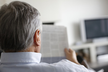 Back view of man reading newspaper at home