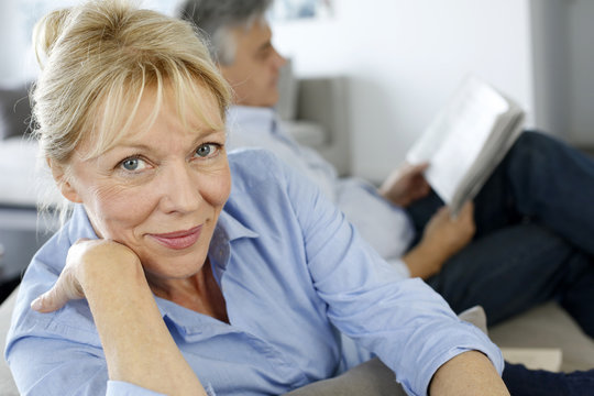 Senior woman sitting in couch, husband in background