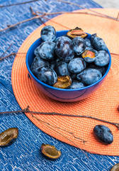 Спелые сливы в синей вазе на оранжевой салфетке
