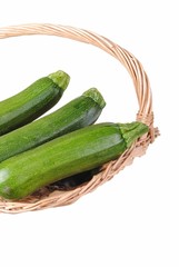 organic courgette in a straw basket, isolated on white