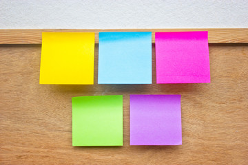 Five colorful sticky notes on wooden board.